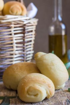 three rolls sitting on top of a wooden table next to a basket with olive oil