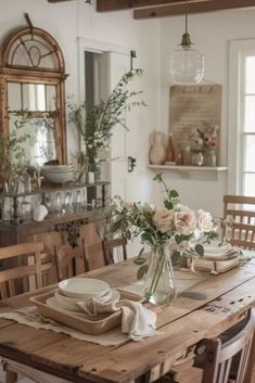 a dining room table with plates and flowers in a vase on the centerpieces