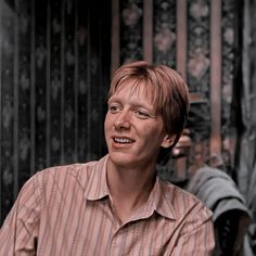 a man sitting in front of a metal fence with his eyes closed and one eye open