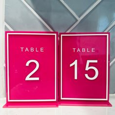 two pink table numbers are displayed against a wall