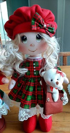 a doll with long blonde hair holding a teddy bear and wearing a red plaid dress