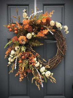 a wreath with orange and white flowers hanging on the front door to give it an autumn feel