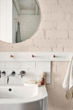 a white sink sitting under a round mirror next to a wall mounted faucet