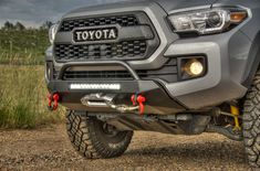 the front end of a gray toyota truck parked on a gravel road with grass and trees in the background