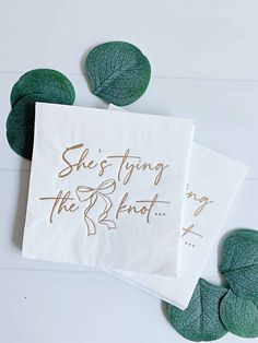 two napkins that say she's tying the knot in gold foil on top of green leaves