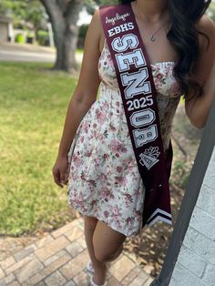 a woman wearing a flowered dress is posing for the camera with her sash around her neck