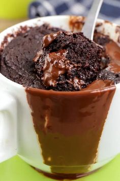 a chocolate dessert in a white cup on a green table with a spoon sticking out of it