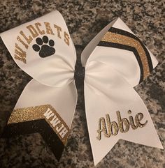 two white and gold cheer bows with an animal paw on the side that says wildcats