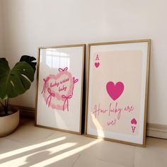 two framed pictures with pink designs on them next to a potted plant and window