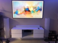 a white entertainment center with speakers and a large painting on the wall above it in a living room