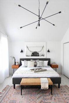 a bedroom with a large bed and lots of pillows on the floor, along with an ottoman