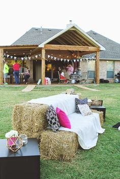 hay bales stacked on top of each other in front of a house with people standing around