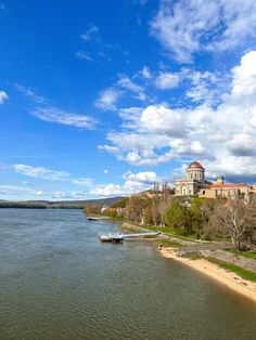 a body of water next to a large building on top of a hill under a cloudy blue sky