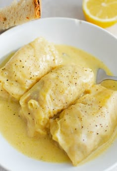 two ravioli stuffed with cheese in a white bowl next to bread and lemon wedges