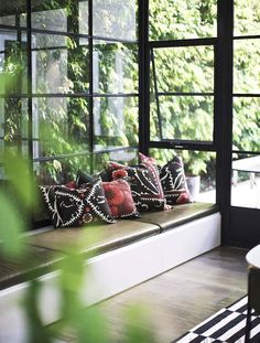 a window seat with pillows on it in front of some plants and trees outside the window