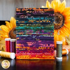 a stack of multicolored fabric next to some spools of thread and sunflower