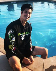 a man sitting on the edge of a swimming pool wearing a black shirt and snoggles