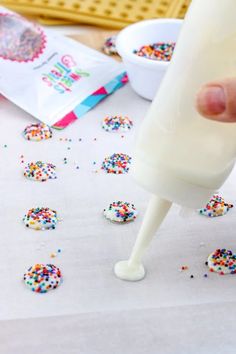 someone is pouring sprinkles onto doughnut holes on a sheet of paper