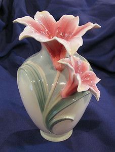 two pink flowers in a white vase on a blue cloth covered table with a blue background