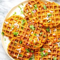 three waffles on a white plate topped with chopped onions and cilantro