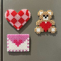 two pieces of bead art are displayed on a refrigerator door, one with a teddy bear and the other with a heart