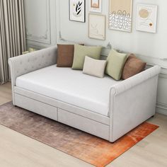 a white couch sitting on top of a wooden floor next to a wall with pictures above it