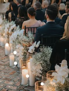 a row of chairs with candles and flowers on the side, as well as people sitting in them