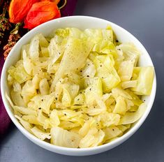 a white bowl filled with cabbage and seasoning on top of a purple table cloth