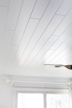 a ceiling fan is hanging from the ceiling in a room with white walls and windows