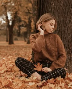 a woman sitting on the ground in front of a tree with leaves all around her