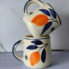 two oranges painted on ceramic mugs sitting side by side