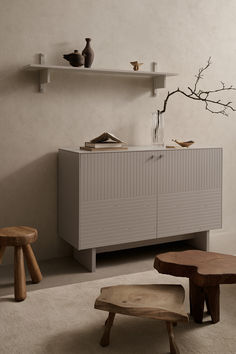 a white cabinet with two wooden stools next to it and a tree branch on the wall