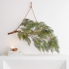 a pine branch hanging from a rope on top of a white shelf next to a candle