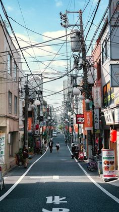 an empty street with lots of power lines above it and people walking on the sidewalk