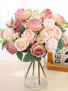 a vase filled with pink flowers on top of a wooden table next to a clock