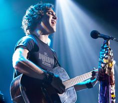 a man holding a guitar and singing into a microphone