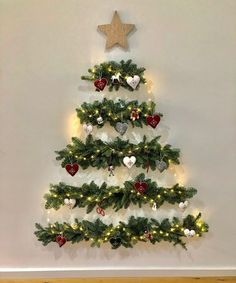 a small christmas tree with lights and ornaments on it in front of a white wall