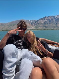 a man and woman sitting on the back of a boat with mountains in the background