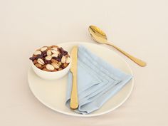 a white plate topped with a bowl of nuts and a fork next to a blue napkin