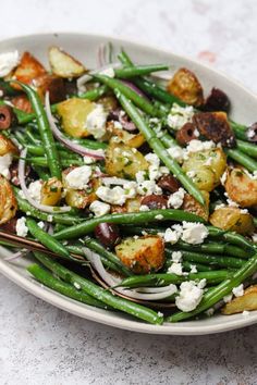 a white plate topped with green beans, potatoes and feta cheese on top of it