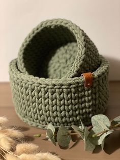 a crocheted basket sitting on top of a wooden table next to dried plants