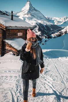 a woman standing on top of a snow covered slope next to a building with a mountain in the background