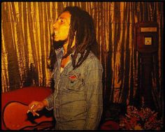 a man with dreadlocks is standing in front of a red couch and gold curtains