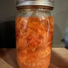 a glass jar filled with liquid sitting on top of a wooden table next to a wall