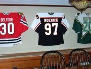 three hockey jerseys are hanging on the wall in a restaurant with wooden tables and chairs