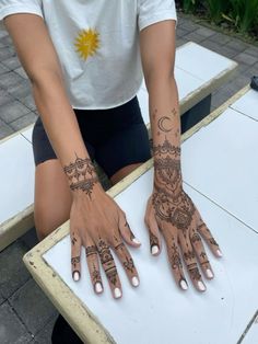 a woman with henna tattoos on her hands sitting at a white table outside in the sun