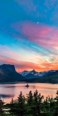 the sun is setting over a lake with mountains in the background and trees around it