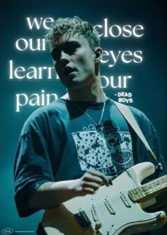 a man holding a white guitar in front of a sign that says we close our eyes learn your pain