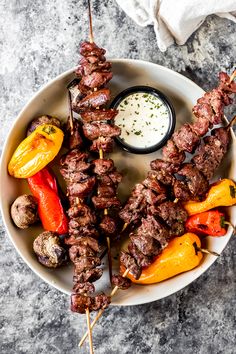 grilled venison kabobs on a white plate with dipping sauce in the middle