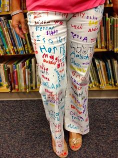 a woman standing in front of a bookshelf with writing all over her pants